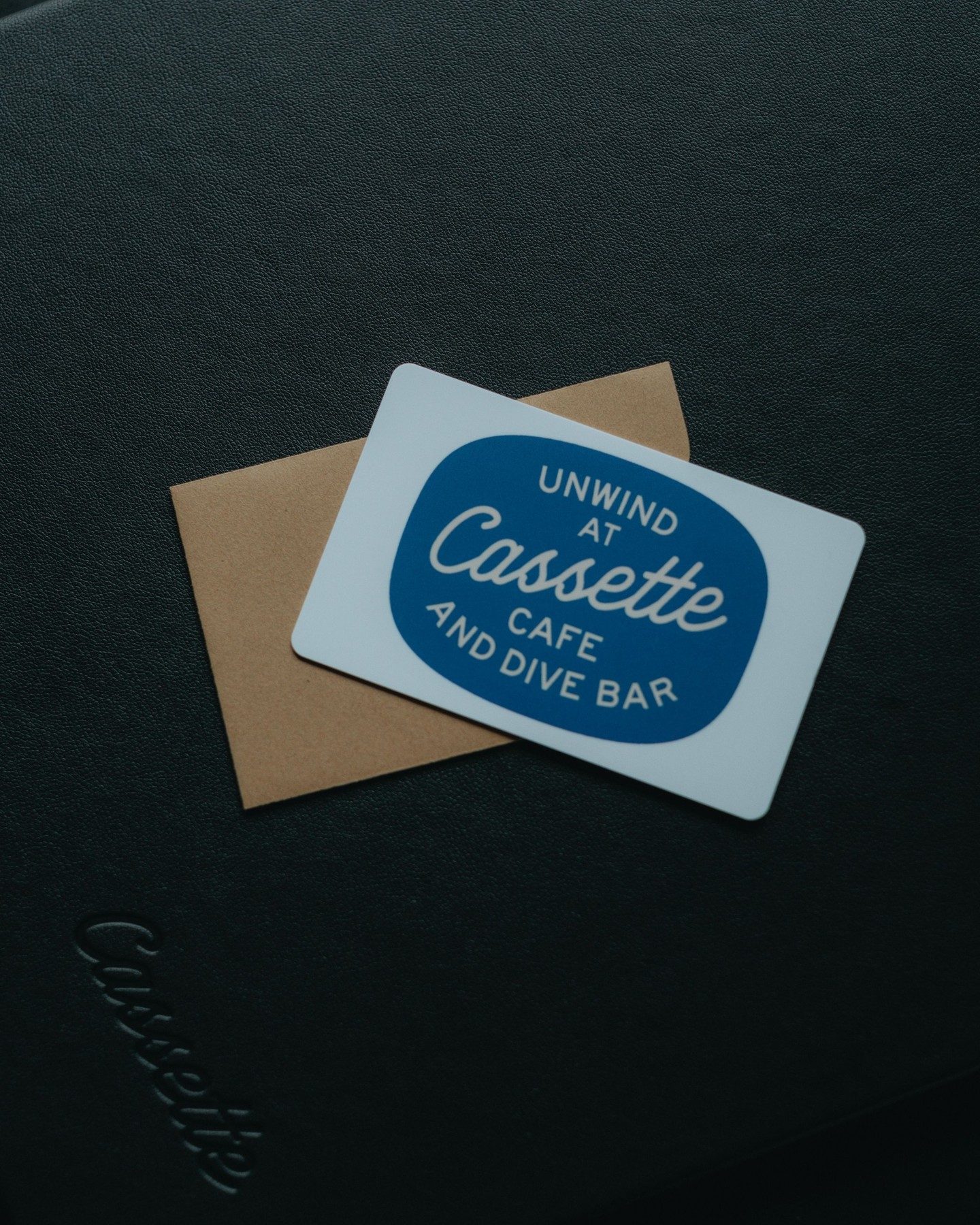The blue Unwind at Cassette gift card on a black table